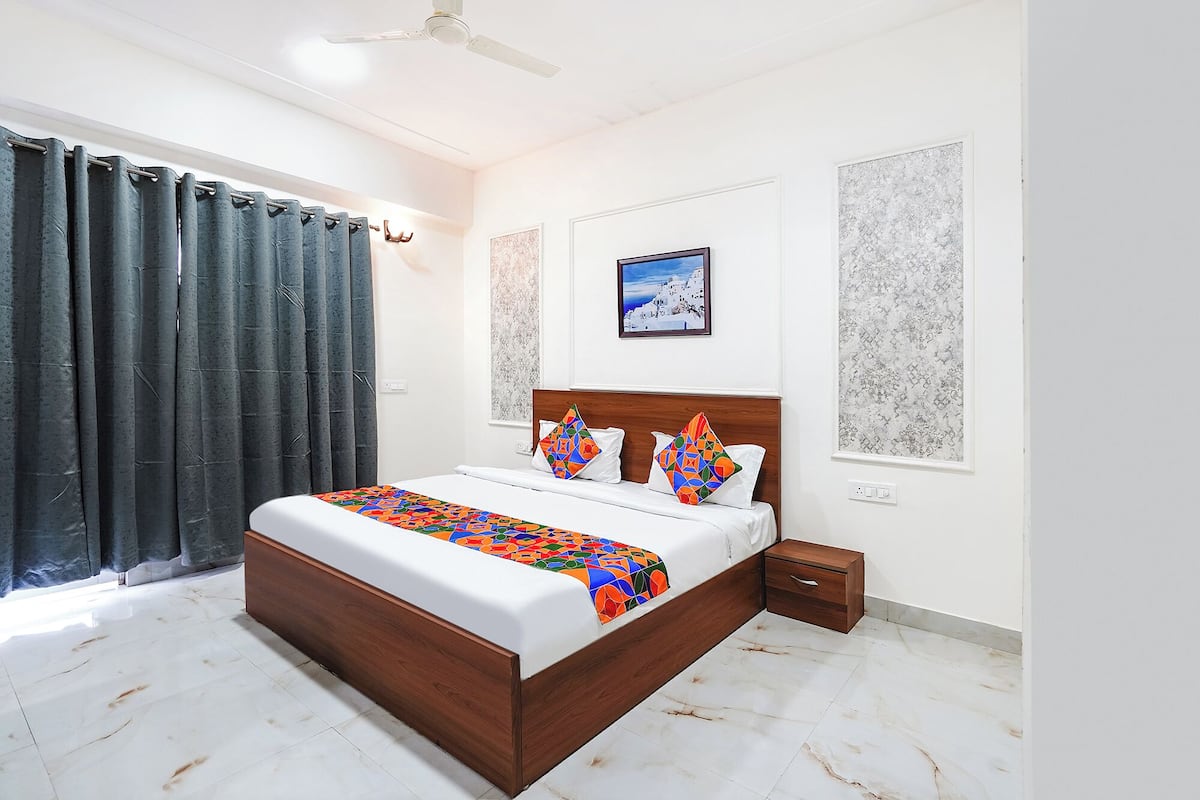 Quarto com cama grande, mesa de cabeceira, ventilador de teto e janela com cortinas.