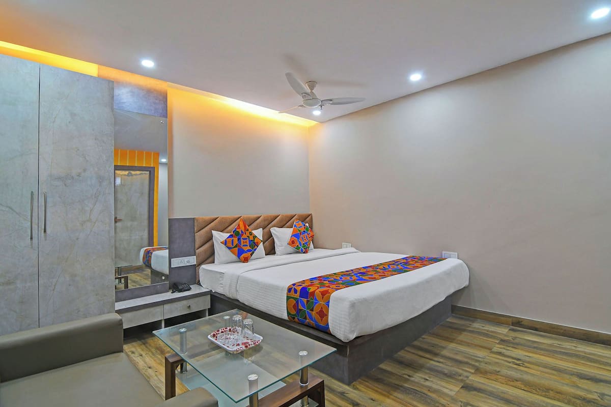A hotel room with a bed, a glass coffee table, a bedside table with a lamp, a ceiling fan, and a large mirror.