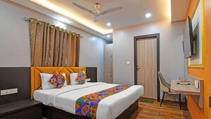 A hotel room with a bed, bedside tables, a desk, a chair, a ceiling fan, and curtains. - Fabhotel Disa (Kolkata)