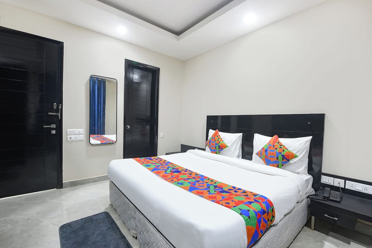 Una habitación de hotel moderna con una cama grande, una mesita de noche, un espejo y una puerta negra.