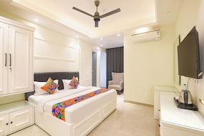 A modern hotel room with a large bed, a chair, a TV, and a ceiling fan. - Fabhotel Heritage Inn Golf Course Rd (Gurugram)
