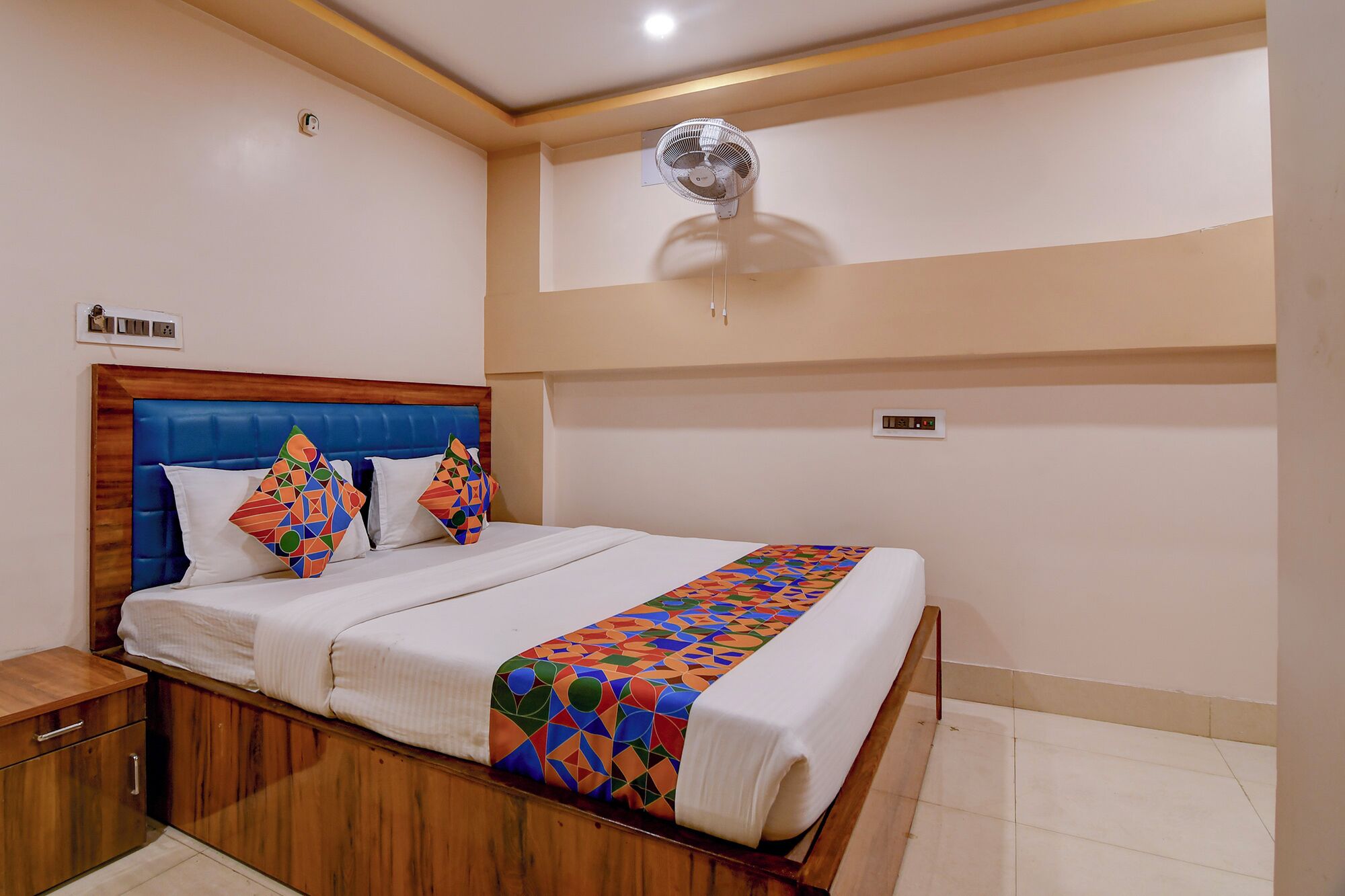 Una cama bien hecha con una colcha de colores y un estampado geométrico, un cabecero tapizado en azul y dos almohadas decorativas.