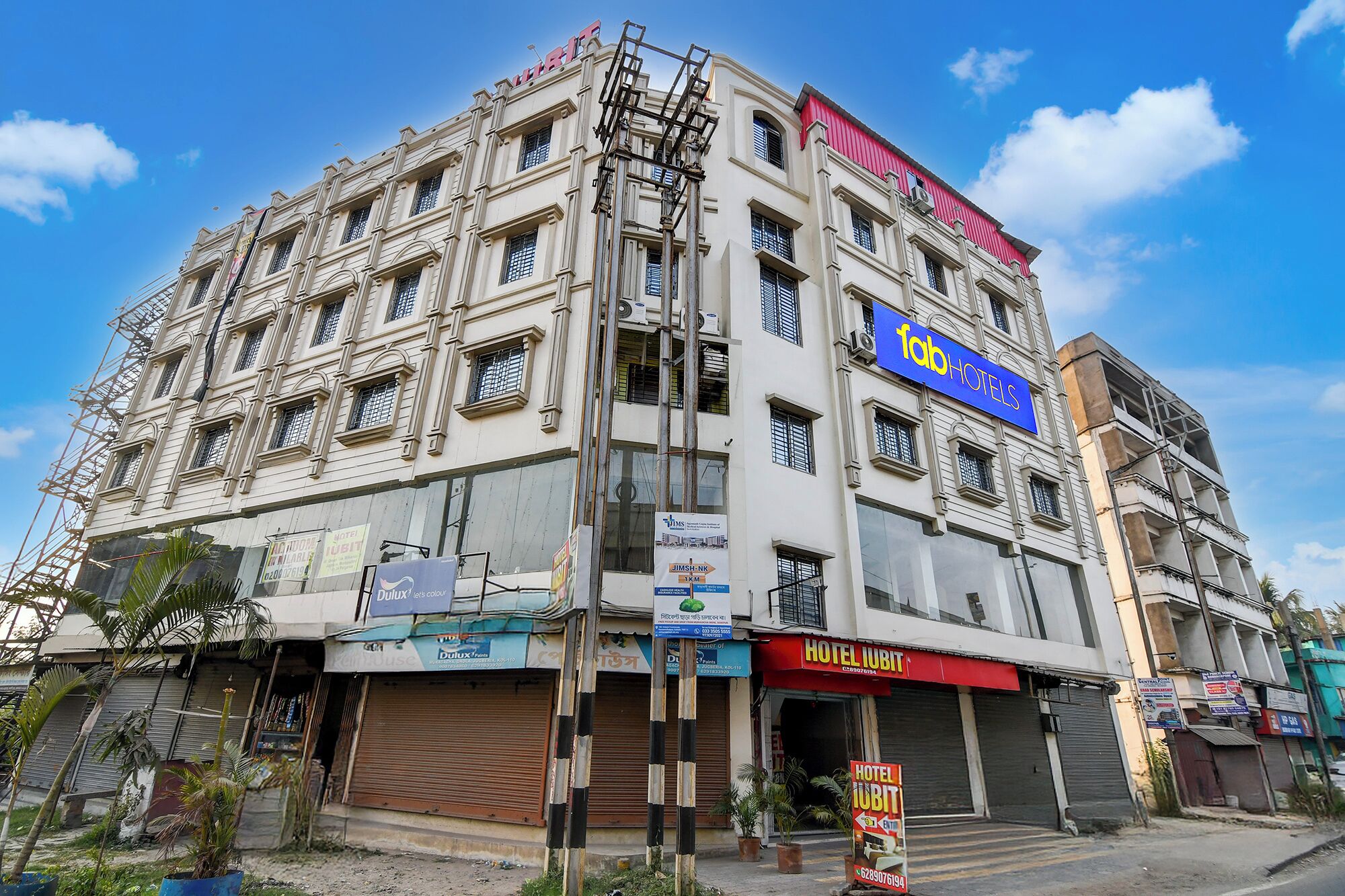 Un edifici de diversos pisos amb un cartell ben visible de 'Hotel Iubit', diverses botigues a nivell del carrer i una tenda vermella.