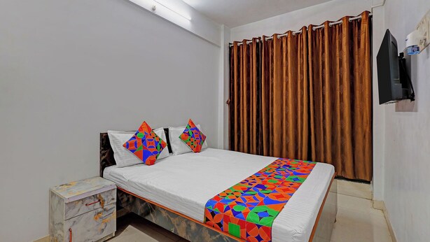 A bedroom with a bed, a nightstand, a TV, and a window with curtains. - Fabhotel Ar Residency (Mumbai)