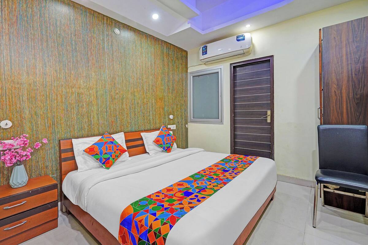 Un dormitorio con cama, mesita de noche, silla, ventana y aire acondicionado.