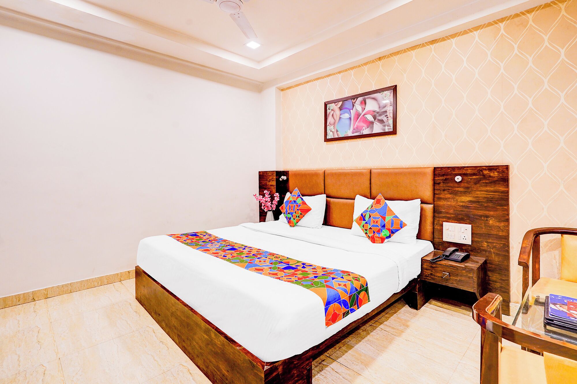 A hotel room with a large bed, a wooden headboard, a nightstand with a phone, and a wall-mounted painting.