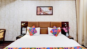 A hotel room with a large bed, two decorative pillows, a nightstand with a phone, a lamp, and a painting of a cityscape. - Fabhotel The Perfect (Lucknow)