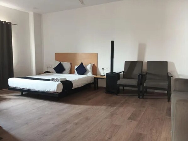 A hotel room with a bed, a chair, a nightstand, and a heater.
