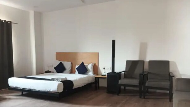 A hotel room with a bed, two armchairs, a nightstand, and a black heater. - Fabhotel Yash Meridion (Jaipur)