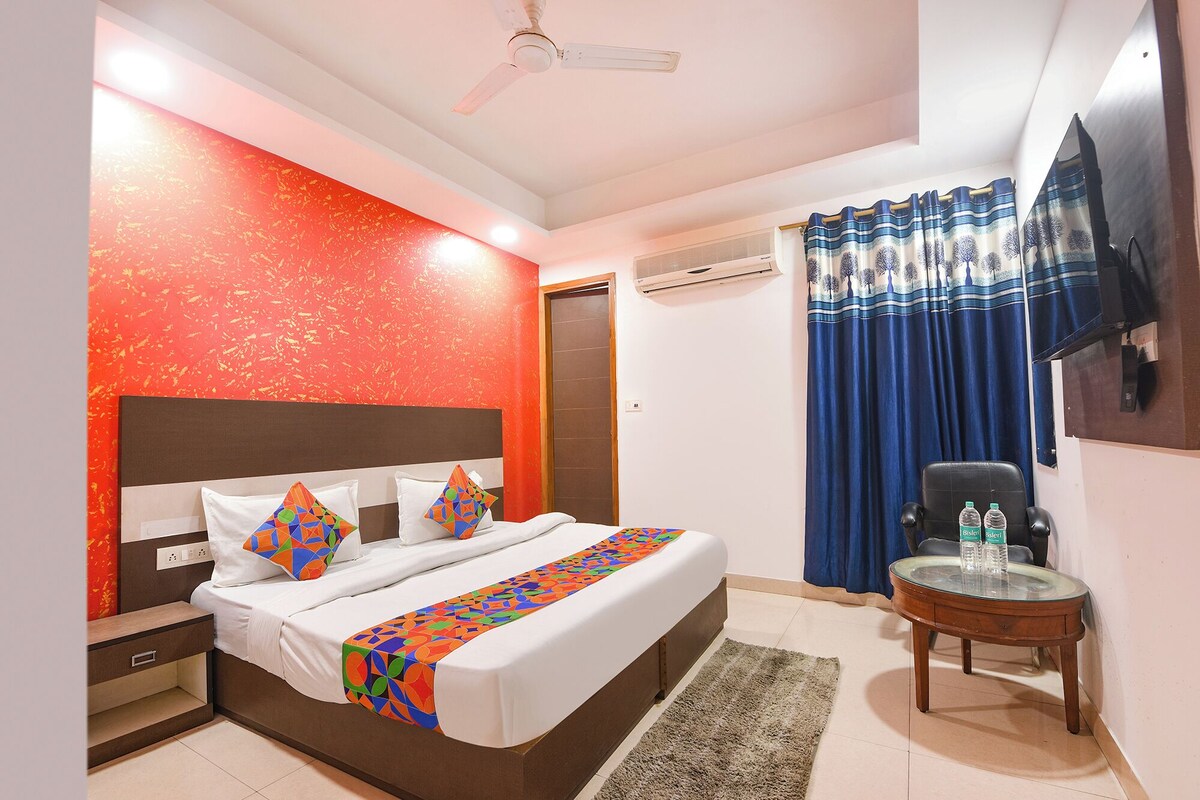 A hotel room with a bed, a desk, a chair, a TV, and a window with curtains.