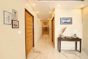 A hallway with wooden doors, a marble floor, framed artwork, and a desk with decorative items. - Fabhotel Rudra (Rishikesh)