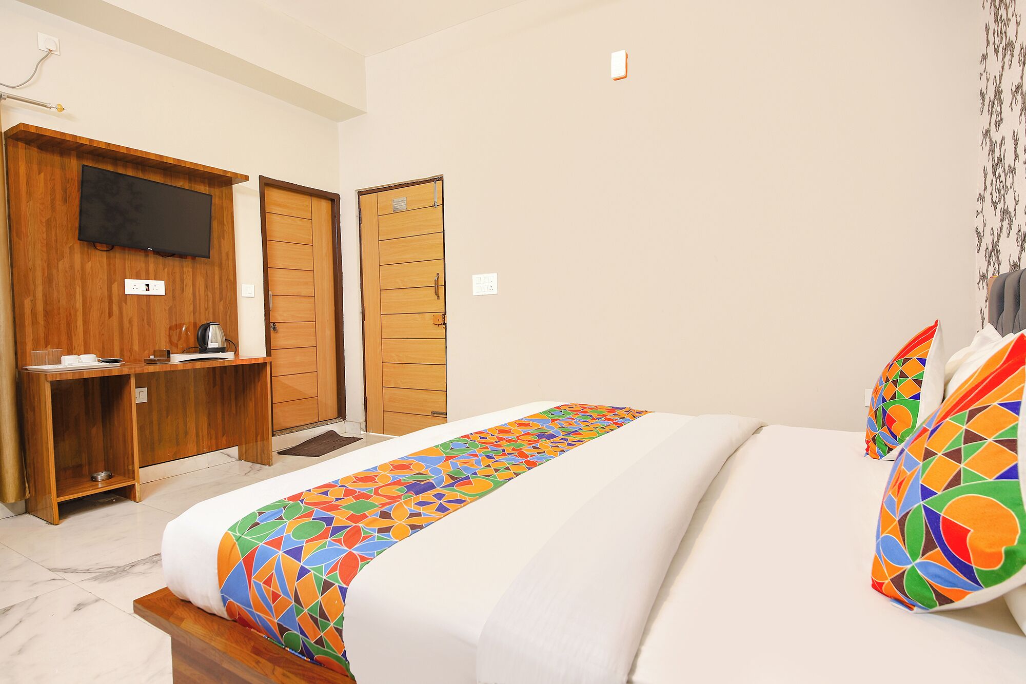 A hotel room with a bed, a desk, a television, and wooden wardrobes.