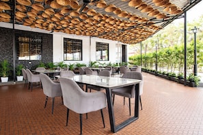 An outdoor dining area with brick flooring, grey chairs, and tables. - Fabhotel Rama (Indore)