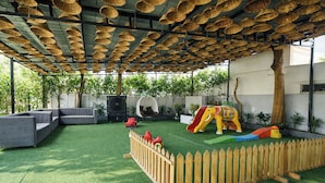 A covered outdoor area with artificial grass, a wooden fence, a slide, and a play structure. - Fabhotel Rama (Indore)