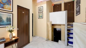 A hallway with a wooden door, framed artwork, a small table with a vase and books, and a whiteboard on the wall. - FabHotel AK Residency (Mumbai)
