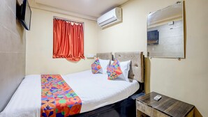 A hotel room with a bed, a bedside table with a phone, an air conditioning unit, a window with curtains, and a mirror on the wall. - FabHotel AK Residency (Mumbai)