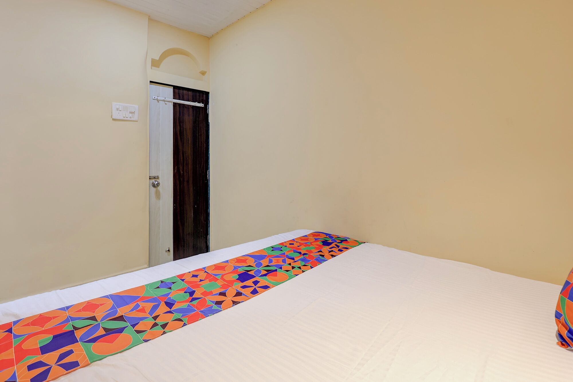 A hotel room with a bed, a door, and a power outlet on the wall.