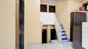 A narrow hallway with a staircase leading to a second floor. The walls are painted in a light yellow, and there are wooden doors with numbers on them. - FabHotel AK Residency (Mumbai)
