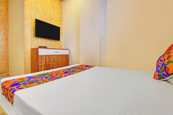 A hotel room with a bed, a wooden wardrobe, a flat-screen TV mounted on the wall, and a colorful patterned bedspread. - Via Kamal Stay Inn (Pune)