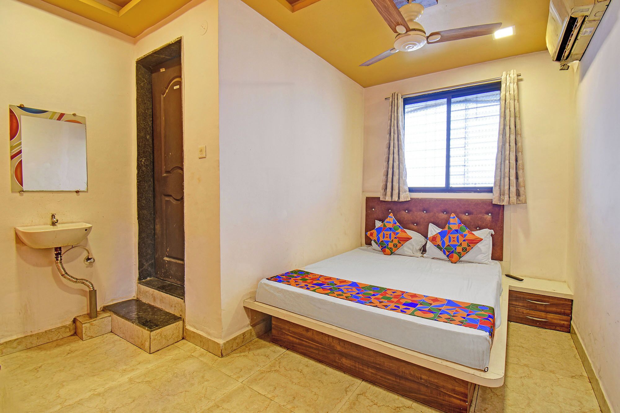 Une chambre à coucher avec un lit, une fenêtre avec des rideaux, un ventilateur de plafond et un lavabo.