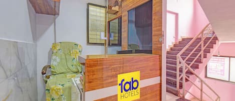 A hotel reception desk with a wooden finish and a 'fab hotels' logo. A chair with a floral cover is visible to the left.