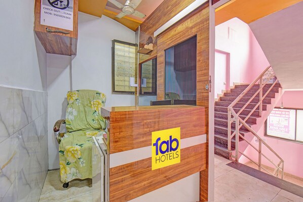 Un mostrador de recepción de hotel con detalles de madera y el logotipo de 'fab hotels'. Se ve una silla con funda estampada a la izquierda.