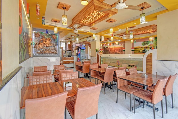 A restaurant interior with wooden tables and chairs, decorative ceiling panels, and a mural on the wall.