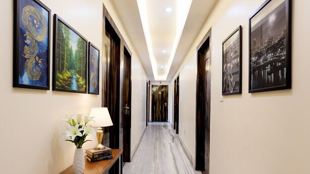 A hallway with framed artwork on the walls, a wooden console table with a lamp and books, and a marble floor. - FabHotel Om Guest House & Banquet (Kolkata)