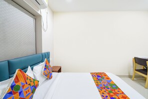 Una camera d'albergo con un letto, una testata blu, un comodino in legno e una sedia.