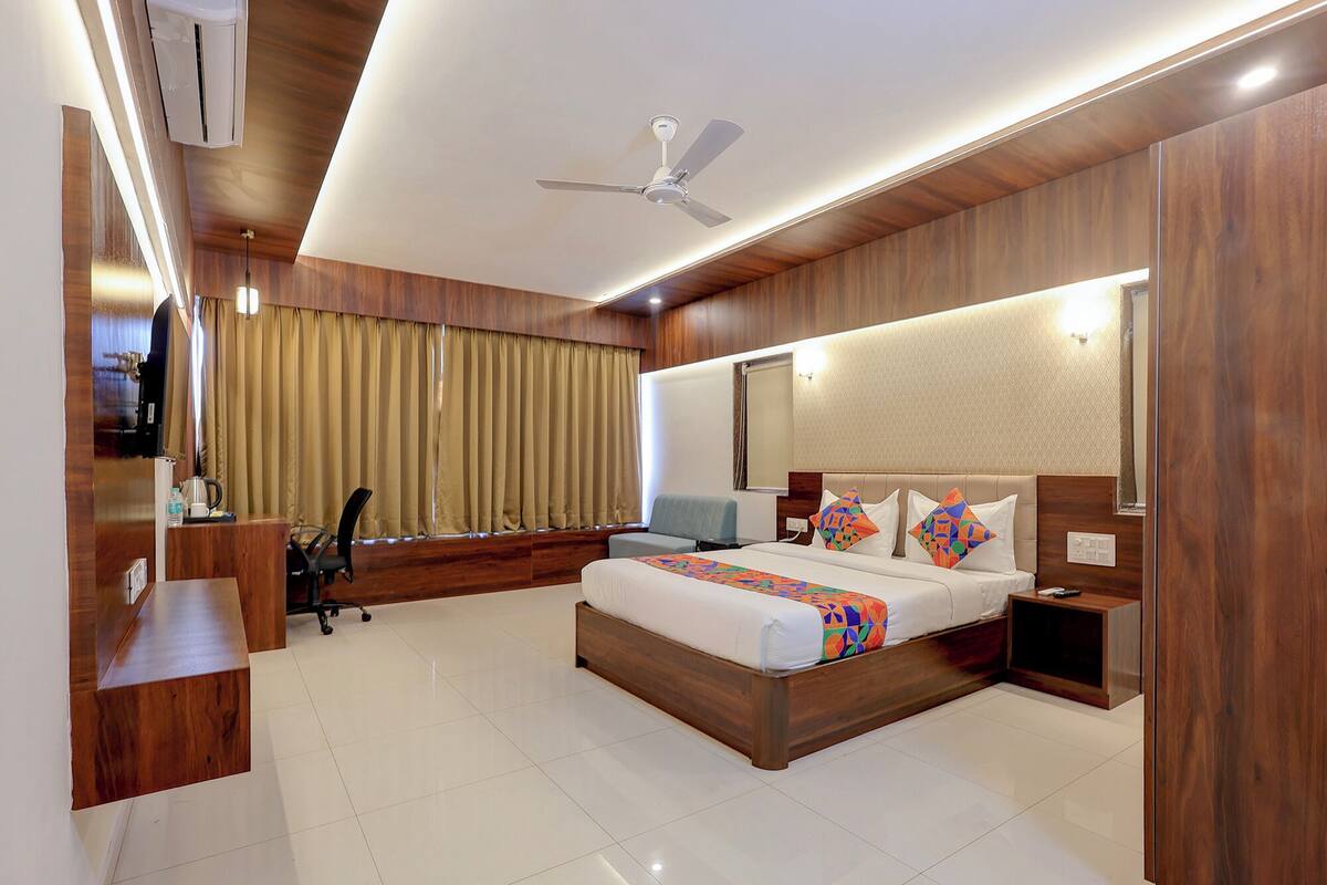 A modern hotel room with a large bed, a desk, a chair, and a ceiling fan.