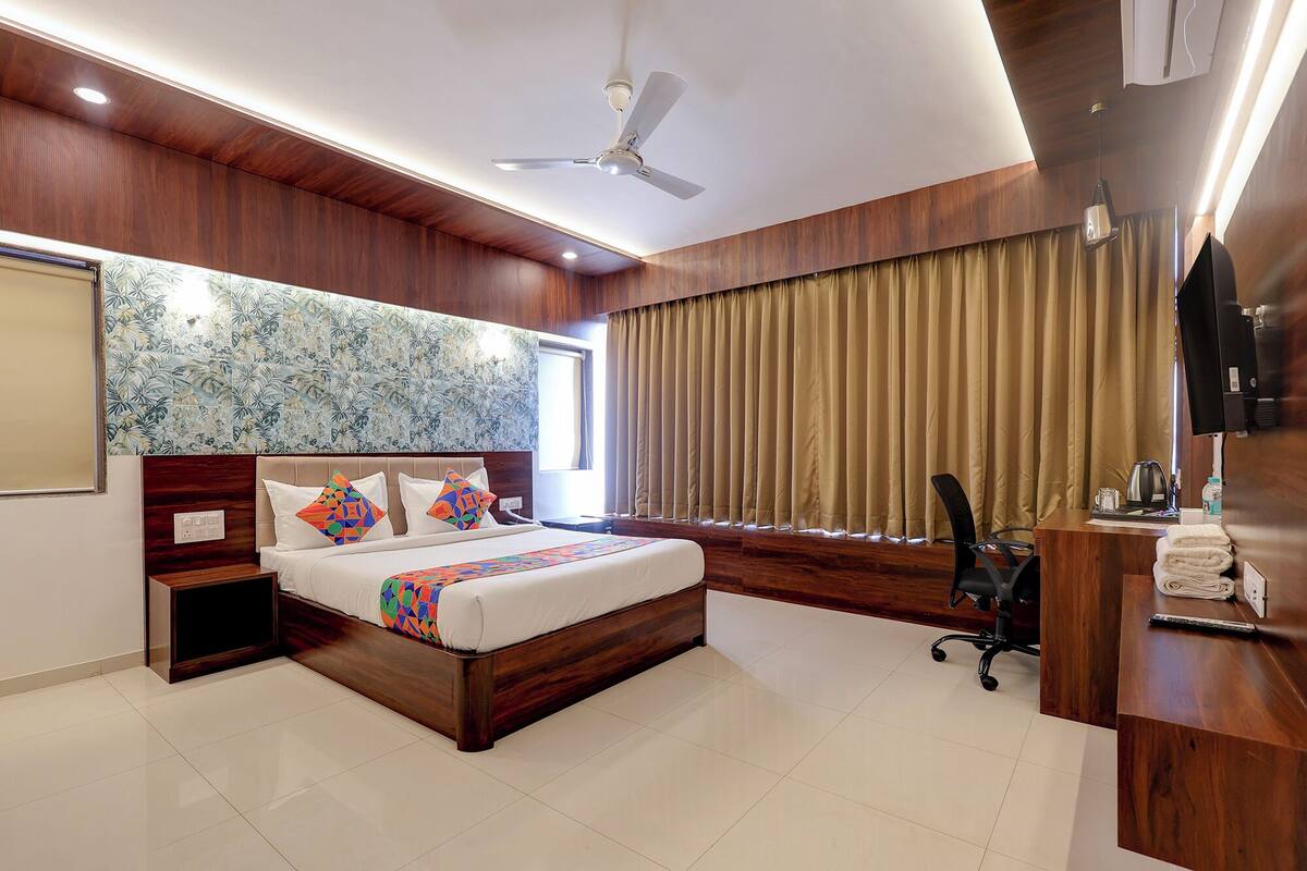 A hotel room with a bed, a desk, a chair, a ceiling fan, and a large window with curtains.