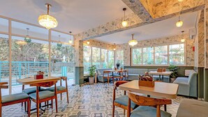 Un café acogedor con mesas y sillas de madera, ventanas amplias que ofrecen vistas al exterior y un papel tapiz con diseño.