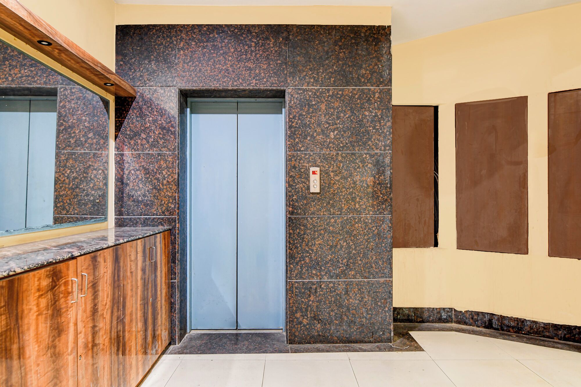 Um elevador moderno com painel de controle, um balcão de recepção de madeira e uma parede com padrão marmorizado.