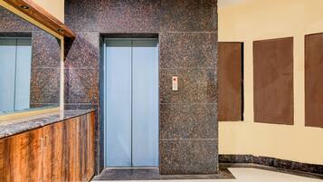 Um elevador moderno com painel de controle, um balcão de recepção de madeira e uma parede com padrão marmorizado.