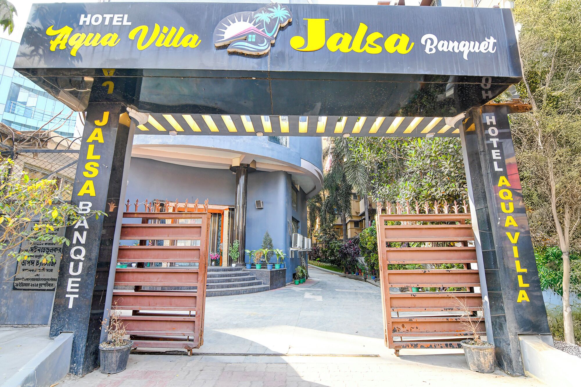 La entrada al Hotel Aqua Villa y al salón de banquetes Jalsa, con un diseño moderno y un camino que conduce al edificio.