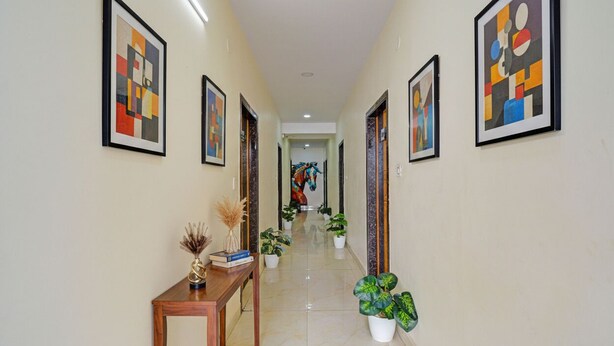 A hallway with framed abstract art, a wooden console table with decorative items, potted plants, and a view into another room with a colorful mural. - Fabhotel La Vista Inn Grand (Hyderabad)