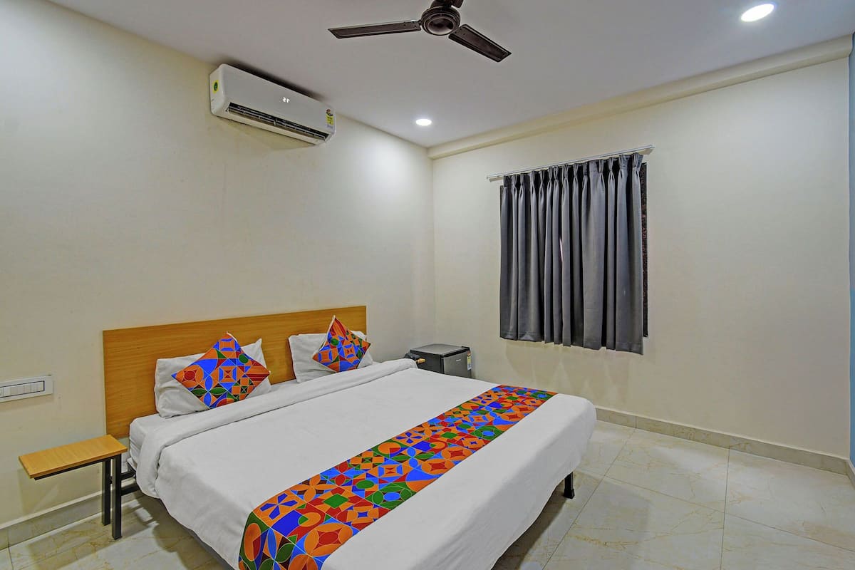 Una habitación de hotel con cama, mesita de noche, aire acondicionado, ventilador de techo y ventana con cortinas.