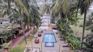 A pool area with lounge chairs and a table, surrounded by palm trees. - FabHotel Bay Breeze - 800M From Morjim Beach (Morjim)