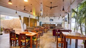 A restaurant with wooden tables and chairs, ceiling fans, and a stone floor. - FabHotel Bay Breeze - 800M From Morjim Beach (Morjim)