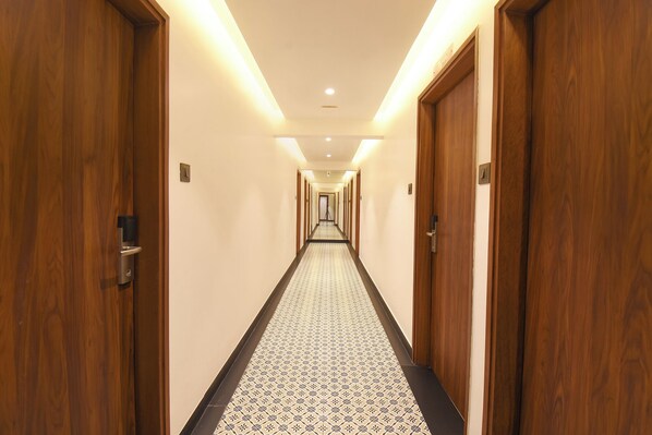 A hotel hallway with wooden doors, a patterned carpet, and recessed lighting.