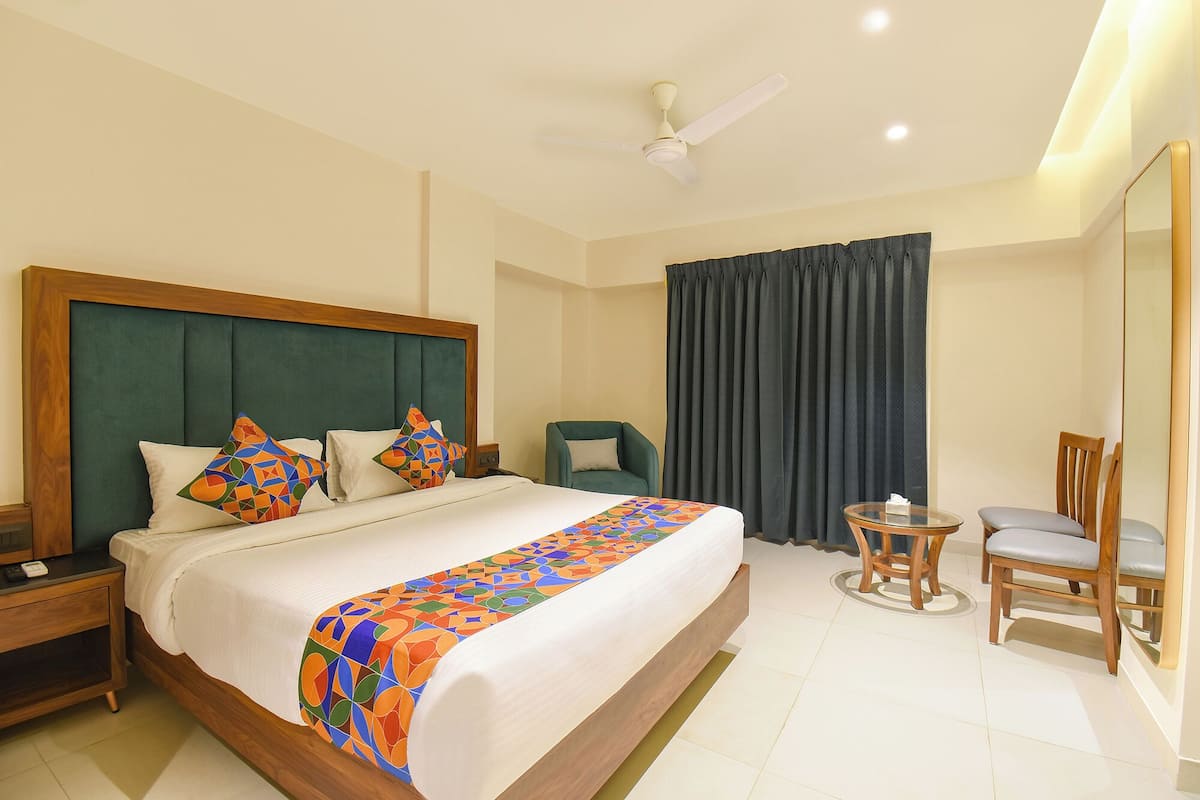 A hotel room with a large bed, a desk, a chair, a small table, and a ceiling fan.