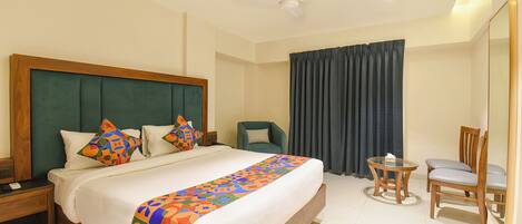 A hotel room with a large bed, a desk, a chair, a small table, and a ceiling fan.