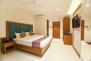 A modern hotel room with a large bed, a wooden nightstand, a television, and a wardrobe.