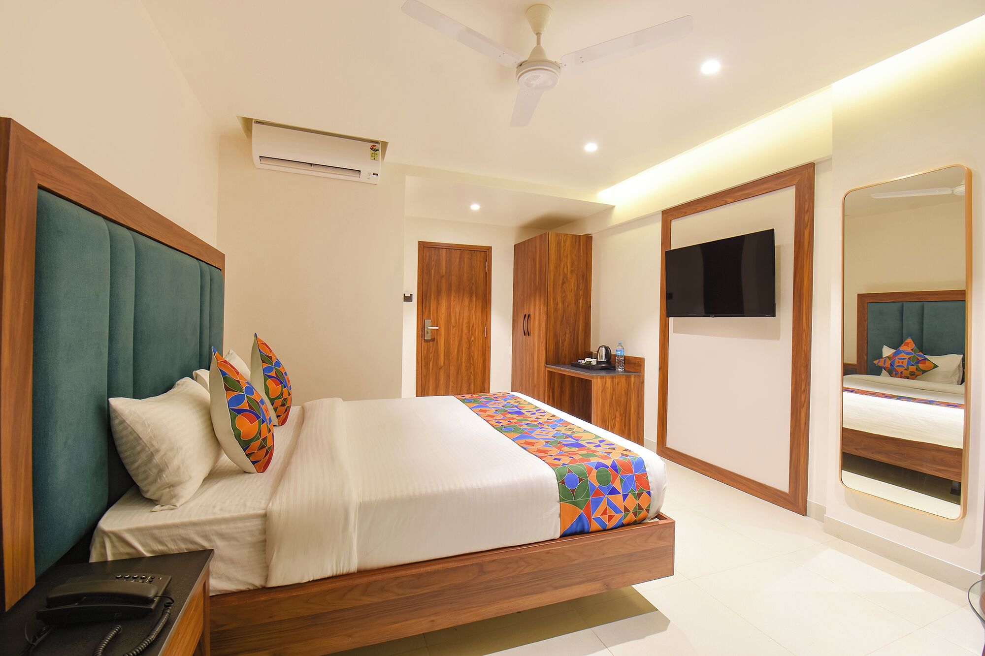 Una habitación de hotel moderna con cama, escritorio, televisor, armario y espejo de baño.