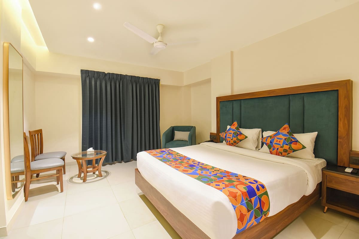 A hotel room with a large bed, a wooden headboard, a nightstand, a chair, a small table, and a ceiling fan.