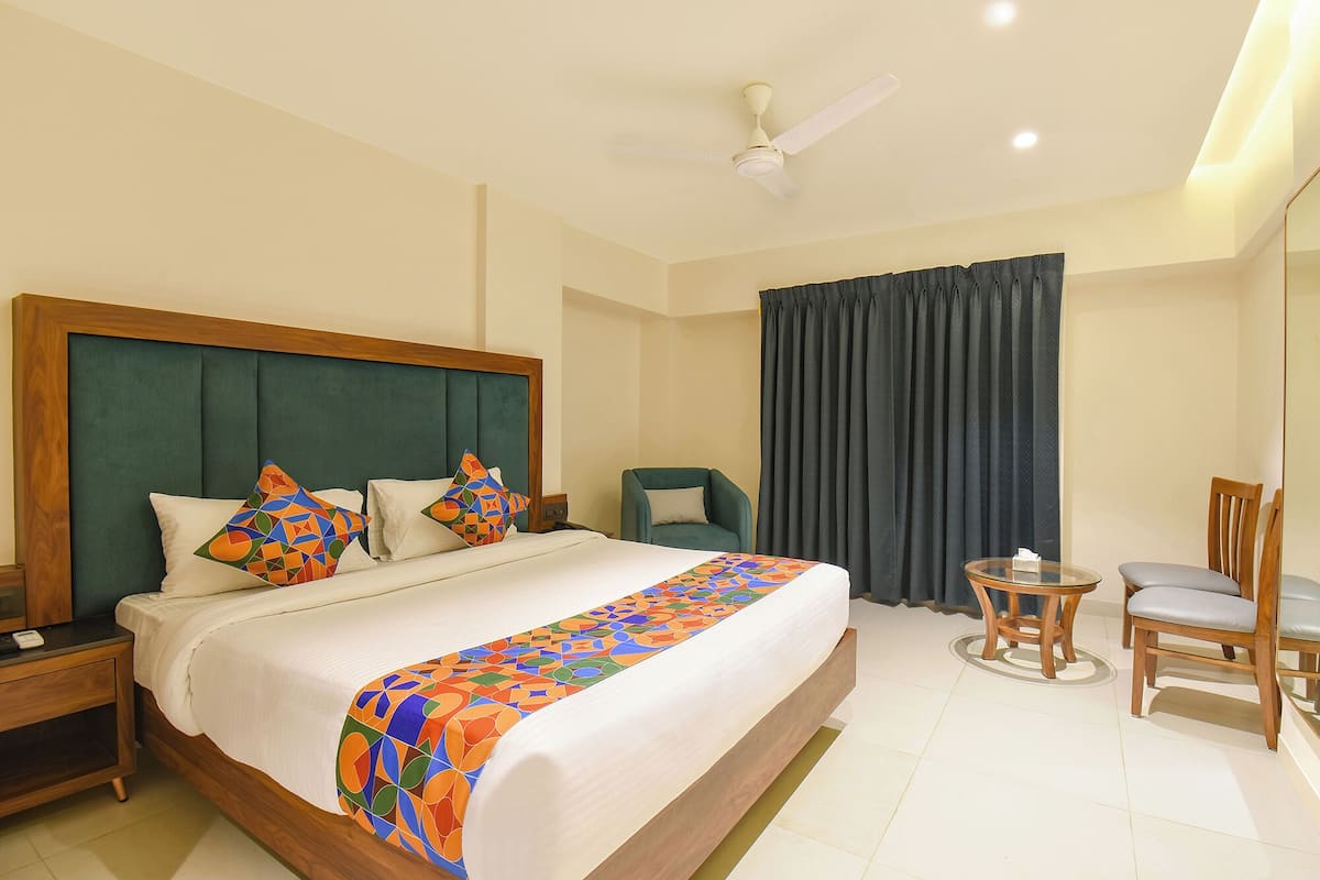 A hotel room with a large bed, a nightstand, a chair, a small table, and a ceiling fan.