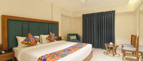 A hotel room with a large bed, a nightstand, a chair, a small table, and a ceiling fan.