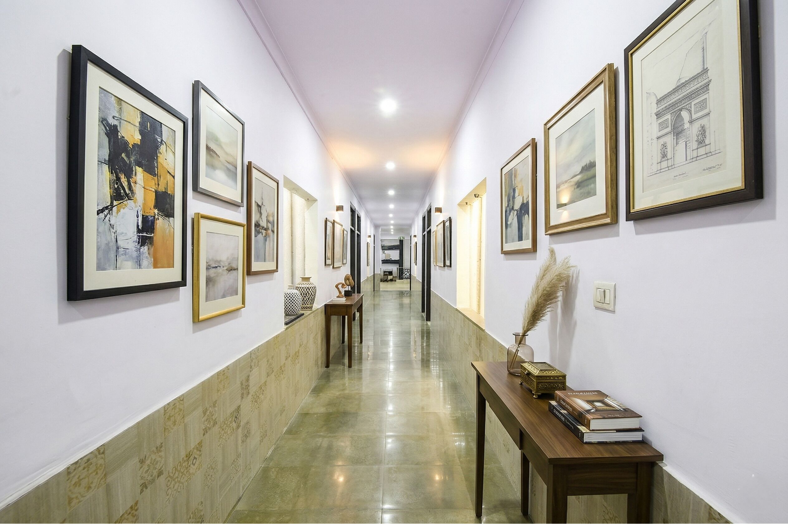 A hallway with framed artworks on the walls, a polished floor, and a wooden table with books and decorative items.