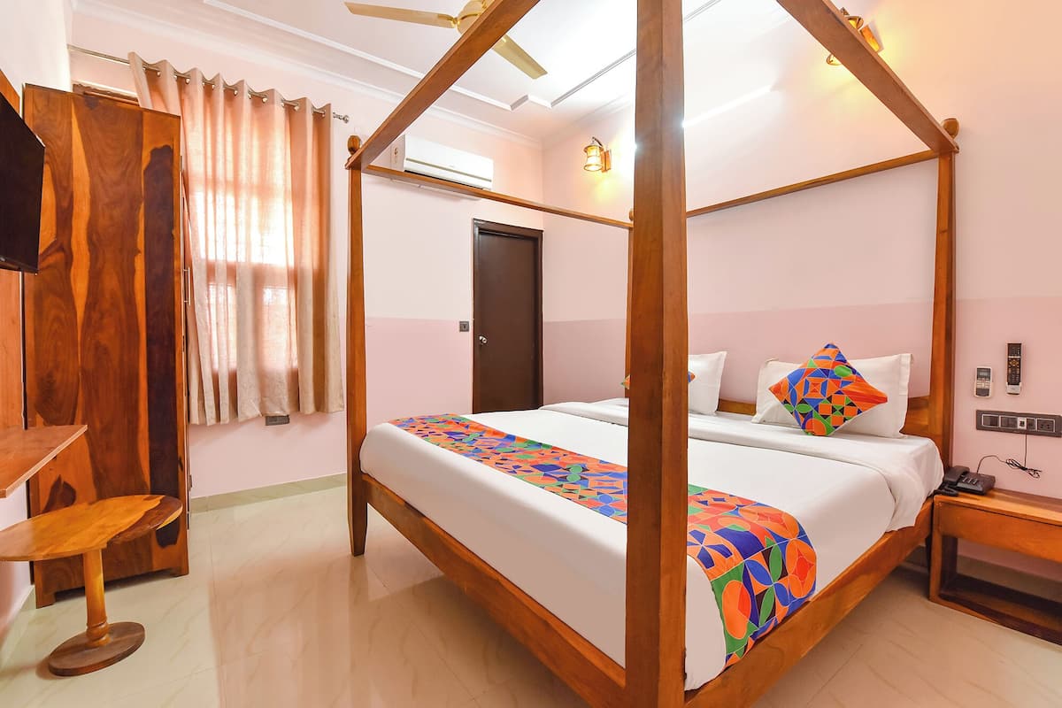 A four-poster bed with a colorful geometric bedspread, a wooden nightstand with a phone, and a desk with a chair in a hotel room.