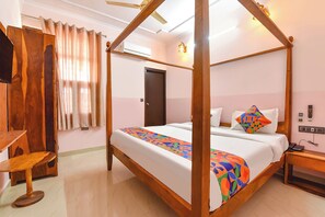 A four-poster bed with a colorful geometric bedspread, a wooden nightstand with a phone, and a desk with a chair in a hotel room. - Fabhotel D7 (Jaipur)